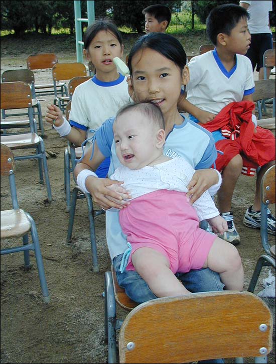 "예쁜 우리 아기" 한 학생이 어린이를 안고 운동회를 지켜 보고 있다. 